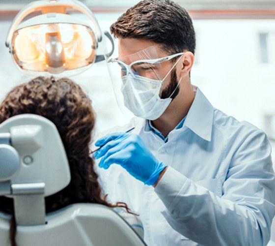 Dentist with blue gloves working on a patient with dark curly hair