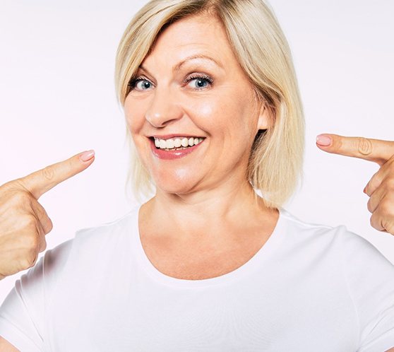 Happy, mature dental patient using mirror to admire her new teeth